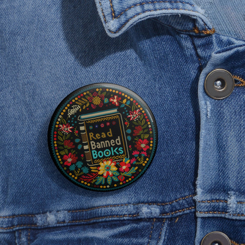 Round black pinback button with vibrant Mexican folk art-inspired embroidery design featuring red, yellow, blue and teal flowers surrounding a gold book spine with "Read Banned Books" text. Literary protest accessory with glossy finish and safety pin backing, available in 2" and 3" sizes.