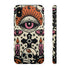 A vertical phone case design featuring a faux crochet texture illusion printed on a cream background. The symmetrical pattern centers on a large black eye with a pink iris and rust-orange sunburst lashes at the top. Below the eye is a black cross surrounded by small black stars. The bottom features a skull with a third rust-orange eye on its forehead. Flanking the skull are two candles with orange flames and rust-colored leaves. The design mimics the look of stitched yarn but is a 2d print.