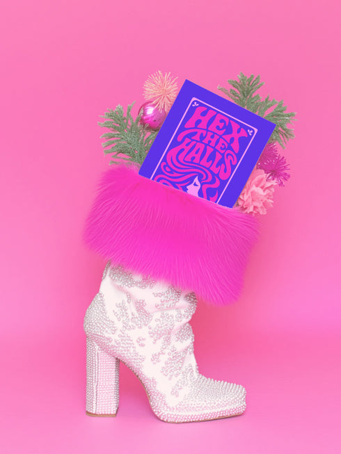 A vertical 5x7 greeting card made from premium 120lb silk cover stock with a slight sheen. The card has a deep purple background with a thin pink border. In the center, the words 'Hex the Halls' are written in a bubbly, psychedelic 70s-style font in shades of hot pink and light pink. Below the text is a stylized pink silhouette of a woman's face in profile with long, flowing, wavy hair. The design is reminiscent of retro witchcraft and groovy aesthetics, perfect for an alternative holiday.