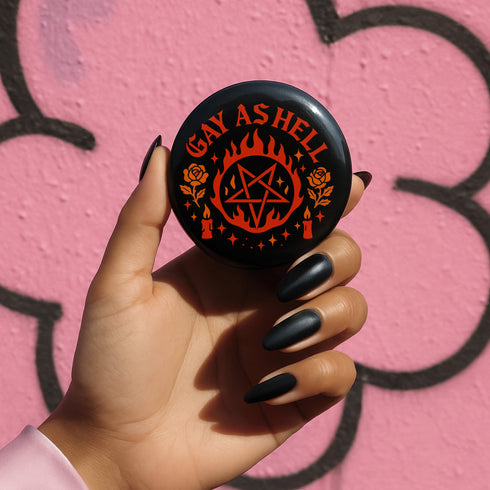 Round glossy pinback button measuring 2.25 inches with bold red graphic design on a black background. Text reads “Gay As Hell” above a red pentagram surrounded by flames, stars, roses, and candles. Made of tinplate with a safety pin back and a scratch-resistant mylar finish. The button features a high-gloss surface and is lightweight and durable, perfect for jackets, bags, or accessories.