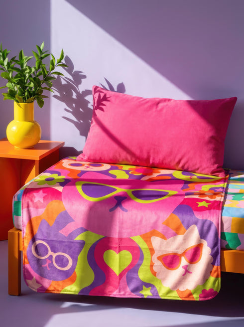 A rectangular velveteen minky blanket with a bright, retro pop art design. The top features a large, hot pink cat head wearing lime green sunglasses in the center. Swirling psychedelic background rays in vibrant orange, purple, and lime green radiate outward. Four smaller cat heads in peach, green, and purple, also wearing glasses, sit in the corners alongside retro flowers, stars, and a lime green heart. The reverse side is a fluffy off-white sherpa fleece.