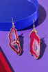 a pair of earrings with a pink and white color scheme, placed on a blue surface.