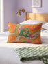 Rectangular 20x12 inch lumbar pillow cover in bright orange featuring printed faux embroidery of a green frog wearing a pink cowgirl hat and pink cowboy boots, lounging on a golden yellow crescent moon shaped like a peeled banana, surrounded by cream and gold sparkle stars and retro wavy stripes. Whimsical cowboy frog design printed on both sides with a hidden zipper, crafted from soft linen look polyester in a funky 70s retro style.