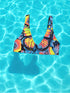 Butterfly-print bikini top with a vivid psychedelic monarch wing design in neon yellow, orange, and pink on a black base. Features a scoop neck, sports bra-style silhouette, and wide shoulder straps. Floating over a bright turquoise swimming pool, this swim top blends Y2K rave energy with bold festival fashion. Perfect for alt-girls, beach rebels, and dopamine dressers craving color-drenched swimwear.