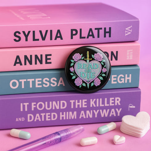 Glossy black pinback button featuring embroidered-style artwork of a pastel purple heart that reads “Read or Die” pierced by a sword and surrounded by roses; shown on books, graffiti, and lace backgrounds.