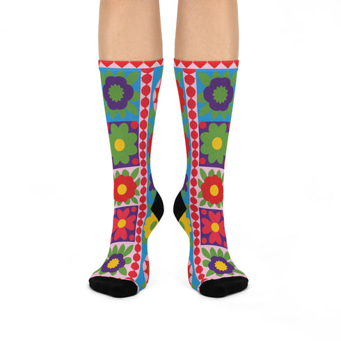 A pair of bright crew socks featuring a vibrant 70s-style maximalist patchwork design. The 2D flat print includes a collage of bold floral motifs in purple, lime green, red, and yellow set against alternating sky blue and light pink square panels. Features a red and white sawtooth border at the cuff and a vertical red scalloped stripe. Reinforced solid black toe and heel. High-quality accessory from black owned shops.