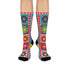 A pair of bright crew socks featuring a vibrant 70s-style maximalist patchwork design. The 2D flat print includes a collage of bold floral motifs in purple, lime green, red, and yellow set against alternating sky blue and light pink square panels. Features a red and white sawtooth border at the cuff and a vertical red scalloped stripe. Reinforced solid black toe and heel. High-quality accessory from black owned shops.