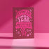A pink card with the text "Another Year Stranger" printed on it, surrounded by various decorative elements such as stars and swirls.