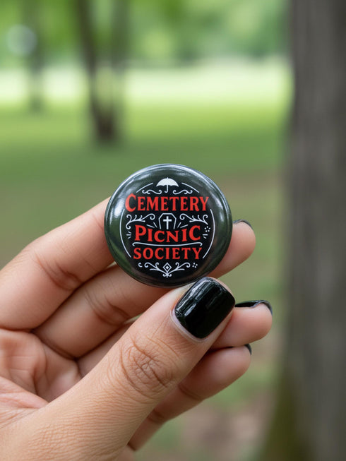 A collection of four glossy black circular pinback buttons featuring striking red and white gothic illustrations. One button shows "Midnight Graveyard Society" text with bats and tombstones. Another reads "Cemetery Picnic Society" with a coffin and umbrella icon. A third features a detailed white skull and red roses with "Memento Mori" text below. The final pin displays "Nocturnal Flower Society" surrounded by floral vines.