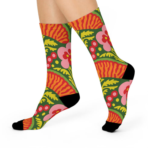 Mid-calf crew sock with a bold retro 70s maximalist botanical print. A deep green base is packed with golden yellow fern-like leaves, pink folk-style flowers with red centers, and clusters of round red and pink berries. Orange and red shell motifs with wavy stripes band the cuff and lower sock. The toe and heel are solid black. The fabric is a soft, stretchy printed knit, made as a one-size unisex statement sock for maximalist and dopamine dressing looks.