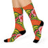 Mid-calf crew sock with a bold retro 70s maximalist botanical print. A deep green base is packed with golden yellow fern-like leaves, pink folk-style flowers with red centers, and clusters of round red and pink berries. Orange and red shell motifs with wavy stripes band the cuff and lower sock. The toe and heel are solid black. The fabric is a soft, stretchy printed knit, made as a one-size unisex statement sock for maximalist and dopamine dressing looks.