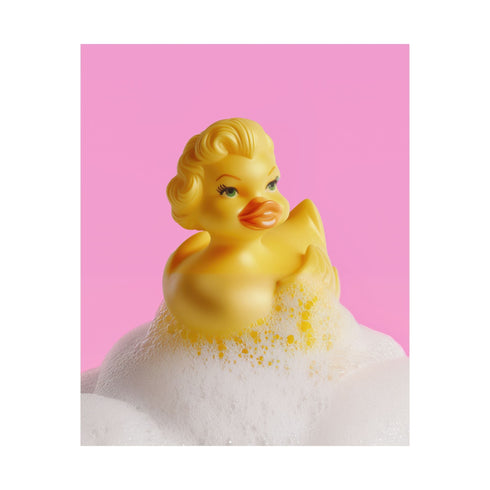 A fine art print of a glamorous rubber duck styled like Marilyn Monroe, with short curled blonde hair and soap bubbles. Displayed in a gold ornate frame against a pink wall with orange bead curtains.