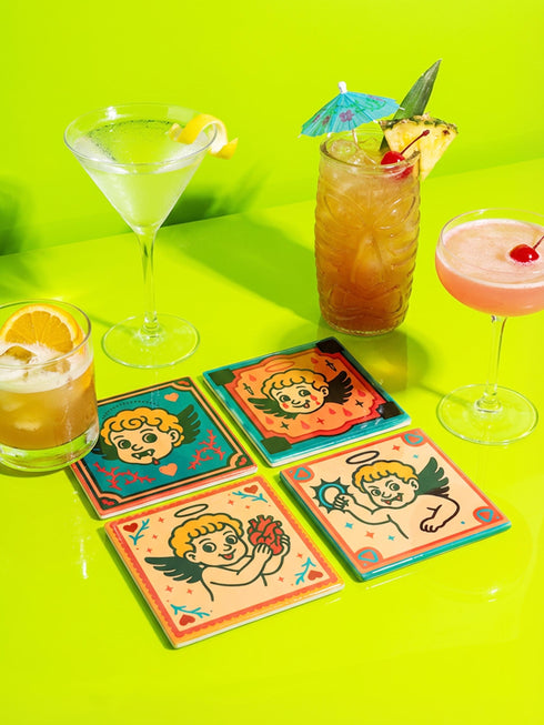 Set of four square ceramic coasters featuring a vampire cupid design in a pastel goth and traditional tattoo art style. The first coaster shows a fanged cherub on a teal background with red vines. The second features a cherub crying blood tears on a red background with daggers. The third depicts a cherub holding an anatomical heart on a peach background. The fourth shows a cherub with a spiked ring. Glossy glazed finish with cork backing. Ideal for spooky home decor and anti-valentine gifts.