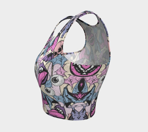 A sleeveless cropped tank top made from stretchy performance knit fabric. The all-over print features a dense, scattered pattern of pastel goth and creepy cute motifs over a light background. Graphics include pink and blue bats in flight, floating eyeballs with blue irises, pink skulls, and glossy vampire lips with sharp white fangs and tongues sticking out. The neckline is a high scoop and the armholes are curved. The fabric comes in either a matte finish or a sparkly silver glitter foil.