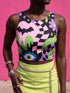 A close-up view of a sleeveless performance knit crop top featuring a vibrant pastel goth all-over print on a solid black background. The repeating pattern includes large black vampire bats flying over dripping, melted slime shapes in neon green. Wavy, warped checkerboard patterns in pastel pink, light purple, and black weave through the design. The graphic is finished with stylized, oversized pastel floral motifs and large open eyeballs staring outward.