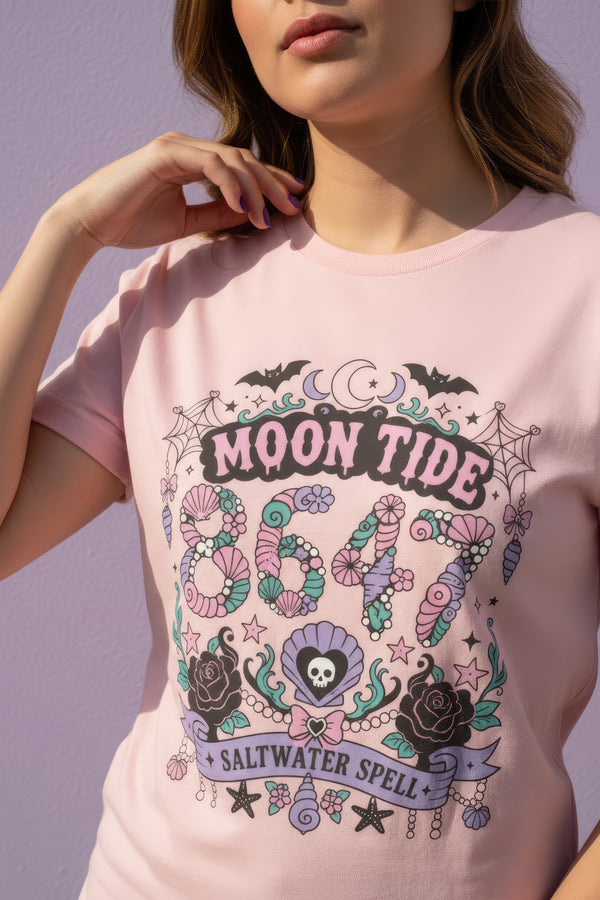 A short sleeve unisex crewneck t-shirt featuring a detailed Moon Tide 8647 graphic centered on the chest. The design includes bats, crescent moons, and spiderwebs at the top, with Moon Tide in a dripping font above a large 8647 rendered in shell patterned bubble numbers. The bottom features a skull inside a scallop shell, roses, and a Saltwater Spell banner. The color palette uses mint green, lilac, and salmon pink with black outlines. The shirt is shown in light pink, lavender, and cream.