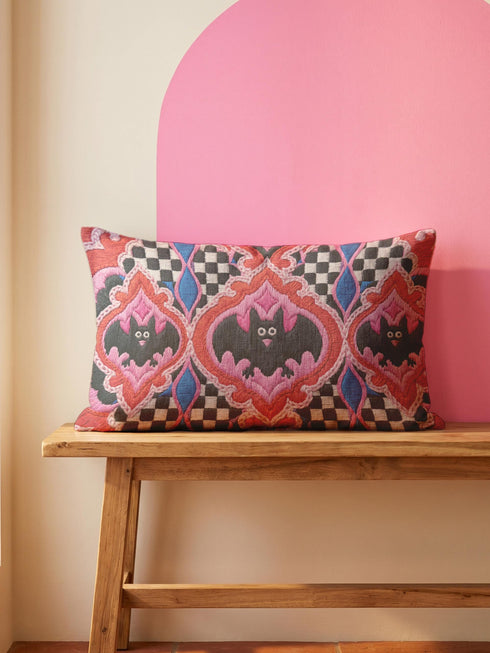 Rectangular 20x12 inch lumbar pillow cover in red featuring printed faux embroidery of three black bats with white eyes and pink noses, each framed in an ornate ogee medallion with pink flame stitch centers, black and white checkerboard accents, and cobalt blue diamonds. Whimsigoth damask bat design printed on both sides with a hidden zipper, crafted from soft linen look polyester for spooky maximalist home decor.