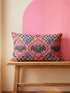 Rectangular 20x12 inch lumbar pillow cover in red featuring printed faux embroidery of three black bats with white eyes and pink noses, each framed in an ornate ogee medallion with pink flame stitch centers, black and white checkerboard accents, and cobalt blue diamonds. Whimsigoth damask bat design printed on both sides with a hidden zipper, crafted from soft linen look polyester for spooky maximalist home decor.