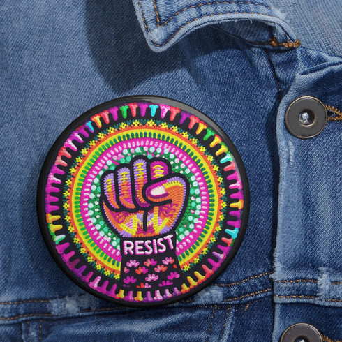 Round pinback button with psychedelic rainbow design featuring a raised black fist surrounded by concentric circles in vibrant pink, orange, green, and yellow. The word "RESIST" appears in white text below the fist, set against black background with flower details. Activist protest pin with glossy finish and safety pin backing.