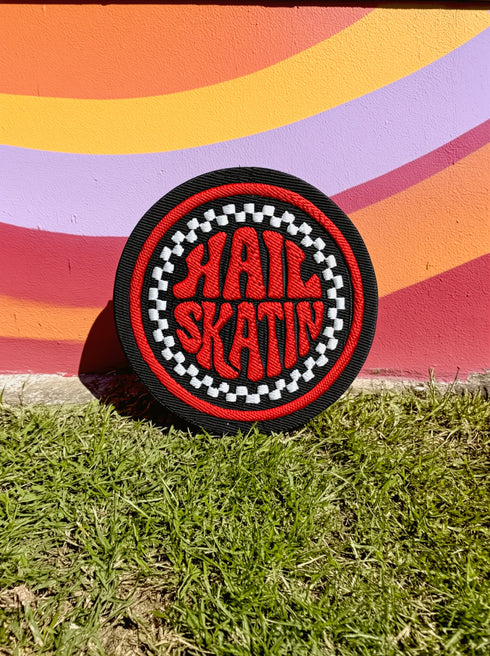 A round, black embroidered patch with a thick, textured merrow border stitched in alternating orange and yellow thread. In the center, the words "PAPERBACK WITCH" are embroidered in a retro 70s-style font. The word "PAPERBACK" is arched across the top in bold orange thread with a thin yellow outline. The word "WITCH" is across the bottom in puffy, bright white thread with a thin yellow outline. Between the words is a central icon of an open book, containing a stylized all-seeing eye.