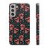 Phone case featuring coral pink apple skulls with green stems and multicolored stars on black background. Gothic alternative design with pastel accents.