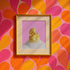 A fine art print of a glamorous rubber duck styled like Marilyn Monroe, with short curled blonde hair and soap bubbles. Displayed in a gold ornate frame against a pink wall with orange bead curtains.