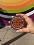 A hand holding a circular patch with the text "SMUT SCHOLAR" printed on it.