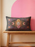 Rectangular 20x12 inch lumbar pillow cover in black featuring printed faux crewel embroidery of a large orange sunburst with a cream face, flanked by pink and yellow crescent moons, a golden moon face above and a pink moon face below, gold stars, blue dots, magenta and blue baroque scroll flourishes, and four corner medallions with golden flowers. Whimsigoth celestial design printed on both sides with a hidden zipper, crafted from soft linen look polyester.