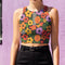 Vibrant retro cropped tank top featuring psychedelic 70s floral pattern with orange yellow purple flowers, black and white checkerboard accents, and wavy green lines on dark background. Body-hugging racerback design made from performance stretch fabric with moisture-wicking properties and UV protection. Perfect for festivals, raves, summer concerts, or bold streetwear styling.