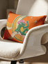 Rectangular 20x12 inch lumbar pillow cover in bright orange featuring printed faux embroidery of a green frog wearing a pink cowgirl hat and pink cowboy boots, lounging on a golden yellow crescent moon shaped like a peeled banana, surrounded by cream and gold sparkle stars and retro wavy stripes. Whimsical cowboy frog design printed on both sides with a hidden zipper, crafted from soft linen look polyester in a funky 70s retro style.