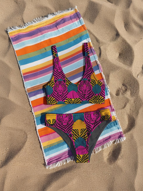 Tropical tiger print bikini bottom with vibrant pink, yellow, and teal psychedelic design. Mid-rise cut with cheeky coverage, double-layered fabric, UPF 50+, and soft, stretchy recycled polyester-spandex blend.