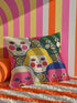 A square decorative pillow cover featuring a faux embroidery pattern of five stylized, expressive doll faces. The central face has yellow hair and pink cheeks. It is surrounded by four other faces in shades of pale beige, green, and bright pink, all with wide staring eyes and open mouths. The design uses intricate, colorful line work to create the illusion of thick woven stitching, but the fabric is a smooth print. Medallions fill the gaps.
