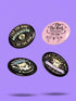 A collection of four retro-style 1.75 inch pinback buttons featuring the text "Tax the Rich" and "Pet the Dogs." Designs include: 1) A black pin with a crystal ball and gold filigree, 2) A pink pin with floral accents and a happy dog, 3) A black pin with a spooky chihuahua holding a bone, and 4) A black pin with a cute devil-horned puppy and lavender banner. High-gloss finish with psychedelic 70s typography. Perfect for battle vests or backpacks. Funny anti-capitalist dog lover gift.