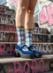 A person wearing blue and white checkered socks and blue platform shoes stands on a set of stairs with graffiti on the steps.