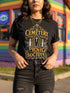 A black unisex crewneck graphic t-shirt featuring an ornate Victorian-inspired emblem printed on the chest in vintage gold and off-white. The centralized, symmetrical design showcases a classic coffin with a cross on the lid, flanked by wrought-iron cemetery gates. Beautiful scrollwork and decorative filigree flourishes surround the bold, retro serif text reading CEMETERY PICNIC SOCIETY. A crescent moon and stars sit at the top, completing this gothic memento mori graphic shirt.