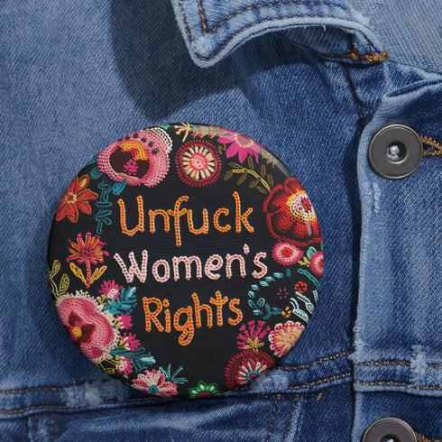 Round pinback button with black background featuring vibrant floral embroidery design surrounding bold orange and white text reading "Unfuck Women's Rights" - feminist protest accessory with glossy finish, safety pin backing, available in 2" and 3" sizes for jackets, bags, and activist wear.