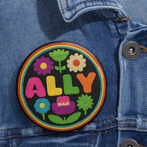Vibrant ALLY pinback button featuring 70s-style embroidered flowers and lettering in pink, yellow, green, and blue against a black background, surrounded by a rainbow border. A colorful statement accessory combining punk activism and retro flower power aesthetics for backpacks, jackets, and protest wear.