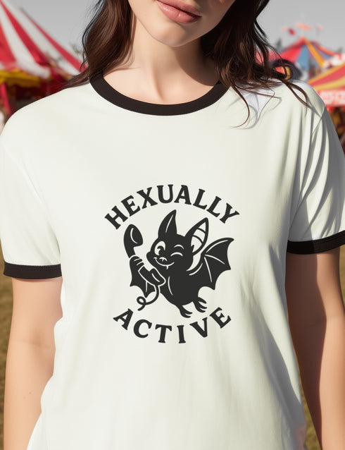 Unisex offwhite and black ringer t-shirt with a bold black graphic of a cartoon bat holding a wand, surrounded by the phrase “Hexually Active.” The design is playful, witchy, and gothic, perfect for lovers of magic, spellwork, hexes, and witch humor. The shirt features contrast collar and sleeves in black for a retro vibe.