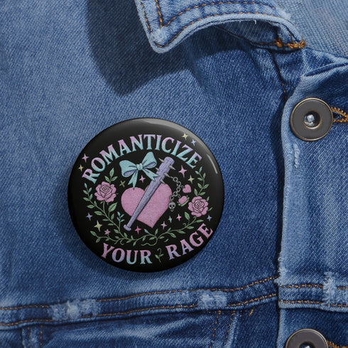 Glossy black pinback button featuring pastel gothic artwork with the phrase "Romanticize Your Rage" in bold white and lavender lettering. The design includes a pink glitter heart, a silver dagger, mint green bow, roses, stars, and delicate vines. Styled against a pink and purple gradient background, this round button blends soft romantic visuals with fierce messaging, perfect for pastel goth, feminist, or alternative fashion aesthetics.