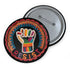 Round pinback metal button with an embroidered-style design on a black background. The center features a raised fist symbol stitched in a multicolored pattern, incorporating rainbow hues and folk-inspired textures. The fist is encircled by a vibrant, lace-like border in shades of blue, orange, and red, resembling intricate embroidery. Below the fist, the word "RESIST" is spelled out in bold, stitched-textured letters in red and orange. The button has a silver metal back with a secure pin closure.