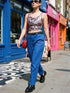 A sleeveless cropped tank top made from stretchy performance knit fabric. The all-over print features a dense, scattered pattern of pastel goth and creepy cute motifs over a light background. Graphics include pink and blue bats in flight, floating eyeballs with blue irises, pink skulls, and glossy vampire lips with sharp white fangs and tongues sticking out. The neckline is a high scoop and the armholes are curved. The fabric comes in either a matte finish or a sparkly silver glitter foil.
