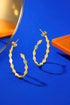 a pair of gold hoop earrings with a geometric design, placed on a blue background.