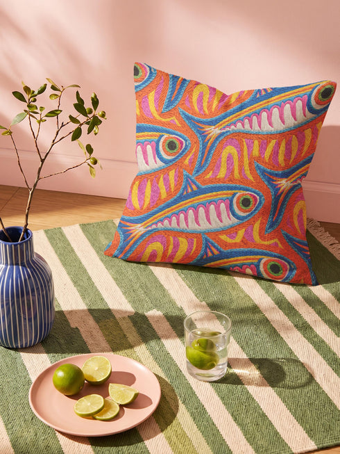 Flat printed square throw pillow cover featuring a faux embroidery texture. The vibrant maximalist design showcases stylized blue, pink, yellow, and white fish swimming in a dynamic, swirling pattern across a bright orange background. The artwork mimics heavy crewelwork yarn and stitching, but the material is a smooth 2D flat print. The pillow is shown as a finished square cover, designed to add bright, colorful eclectic fisherman aesthetic decor to any sofa or seating area.