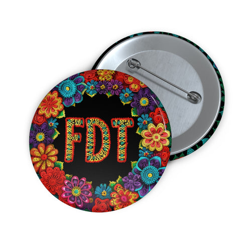 Circular black pinback button with bright 'FDT' lettering in orange/teal surrounded by colorful embroidery-style flowers in red, purple, blue, and yellow. Metal safety pin backing visible on reverse side. Political protest pin with vibrant Mexican folk art-inspired floral design.