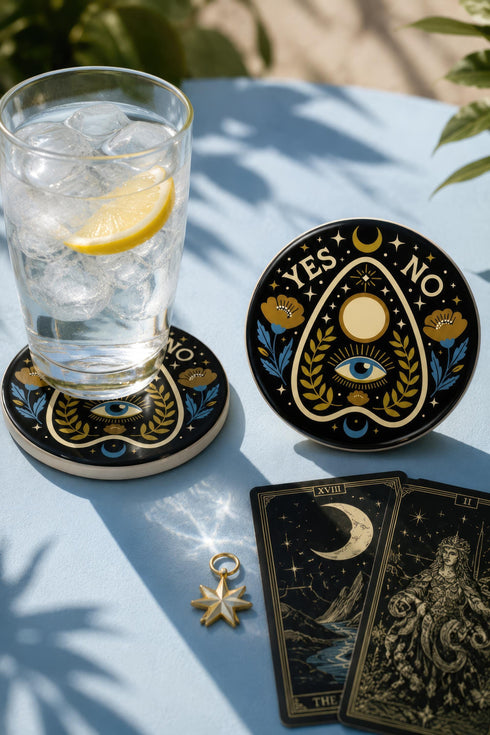 A close-up photograph of a glossy ceramic coaster featuring a Planchette occult design on a deep black background. The symmetrical graphic displays a central blue All-Seeing Eye with gold sunburst lines, topped by a white circle, and flanked by gold flowers with blue stems. At the top, the text "YES" is printed in gold on the left and "NO" on the right. Gold stars and crescent moons are scattered around the perimeter. The flat, round coaster has a highly visible high-gloss glaze.
