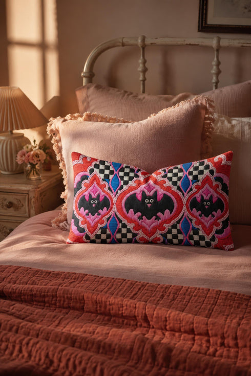 Rectangular 20x12 inch lumbar pillow cover in red featuring printed faux embroidery of three black bats with white eyes and pink noses, each framed in an ornate ogee medallion with pink flame stitch centers, black and white checkerboard accents, and cobalt blue diamonds. Whimsigoth damask bat design printed on both sides with a hidden zipper, crafted from soft linen look polyester for spooky maximalist home decor.