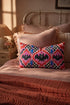 Rectangular 20x12 inch lumbar pillow cover in red featuring printed faux embroidery of three black bats with white eyes and pink noses, each framed in an ornate ogee medallion with pink flame stitch centers, black and white checkerboard accents, and cobalt blue diamonds. Whimsigoth damask bat design printed on both sides with a hidden zipper, crafted from soft linen look polyester for spooky maximalist home decor.