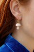 A close-up view of a person's ear wearing a pair of white mushroom-shaped earrings with a gold hook.