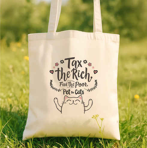 A natural-colored cotton canvas tote bag featuring a bold pink design with a cartoon cat illustration and the phrase “Tax the Rich, Feed the Poor, Pet the Cats.” The artwork is printed on the front side of the bag, which measures 15 inches by 16 inches. The bag includes two sturdy handles for carrying and is made from eco-friendly cotton material, designed for everyday use as a book tote, protest bag, or gift for anti-capitalist cat lovers.