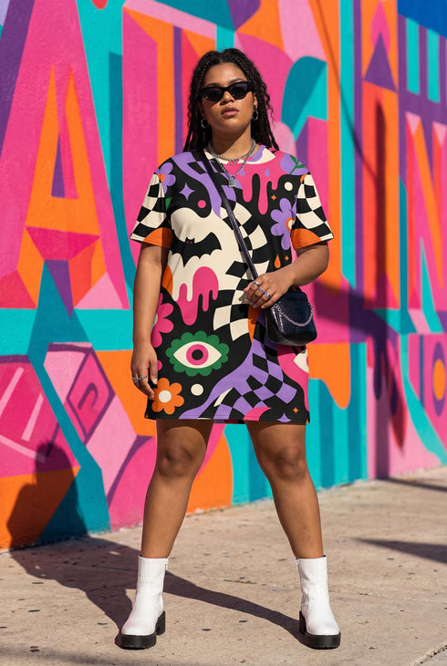 A short-sleeve, above-the-knee t-shirt dress with a relaxed, straight fit and a crew neckline. The dress features a vibrant, chaotic, all-over graphic print. The design includes sections of distorted, wavy black and cream checkerboard, mixed with bold, abstract shapes in bright purple, hot pink, and vivid orange. Scattered throughout the pattern are motifs of hot pink dripping slime, a black bat silhouette, a stylized green eye with a pink iris, and retro pink and purple daisy flowers.